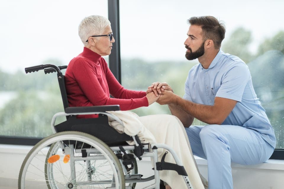 A carer holding the hands of an older woman seated in a wheelchair